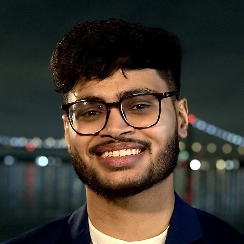 Thanemul Islam smiling in a navy blazer with a lit bridge behind him